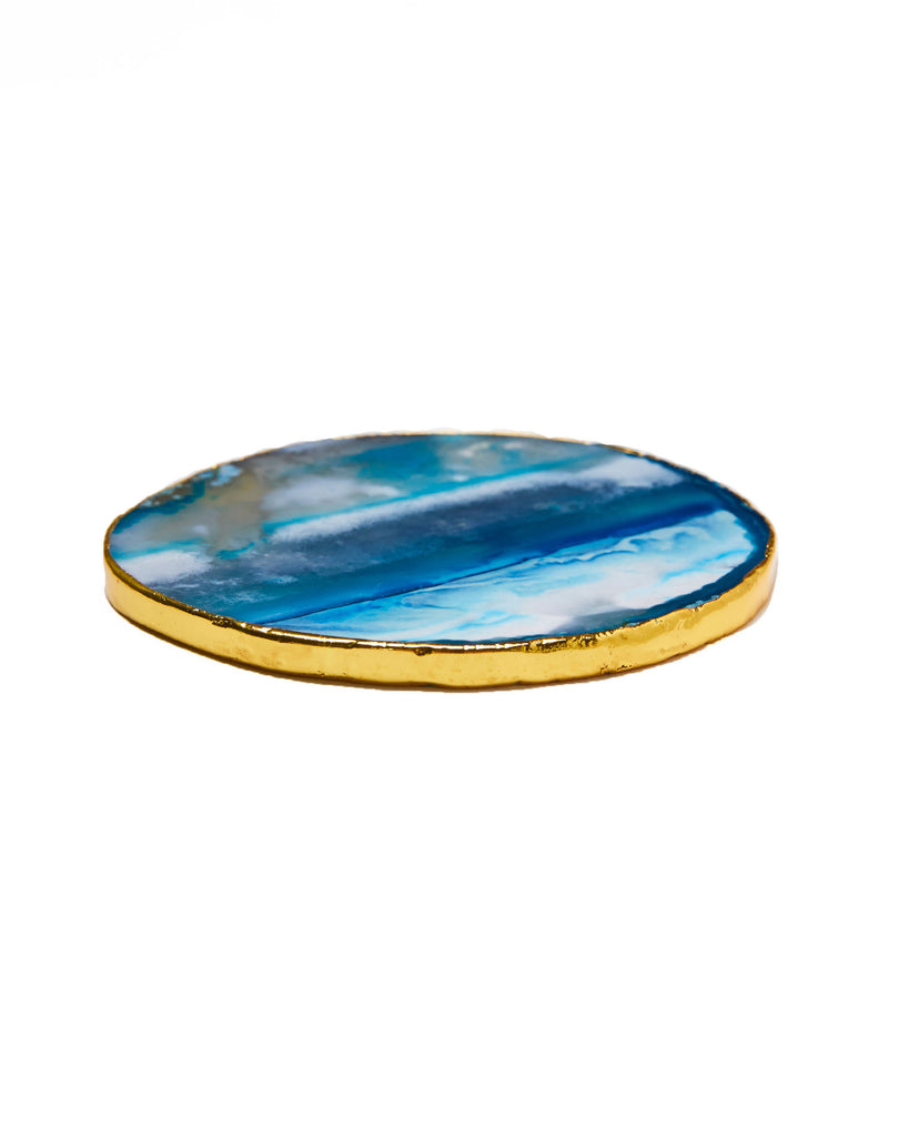 Gold plated blue agate crystal coaster. Our natural crystal coasters are the perfect addition to your dining room or coffee table. With natural blue agate from Brazil, coated in yellow gold plating, this coaster is an easy way to elevate the luxury in your home.  Blue Agate Crystal  100-120mm  Gold Plating  Please note: Due to our crystals being 100% natural, shape and colour patterns will vary.